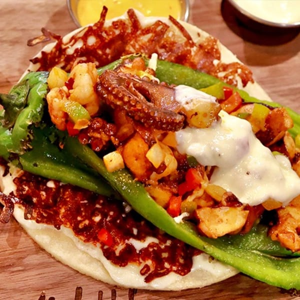 A Culichis Urban Kitchen taco with octopus, shrimp, vegetables, and melted cheese on a tortilla.