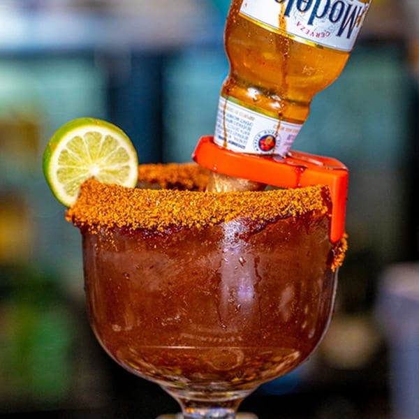 Michelada with a lime slice and an inverted Modelo beer bottle, rimmed with chili powder.