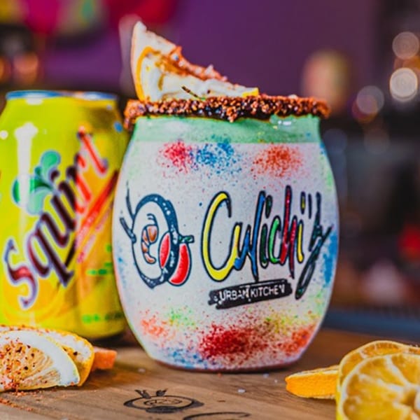 A colorful Culichis Urban Kitchen branded cup with a lemon slice and a Squirt soda can.